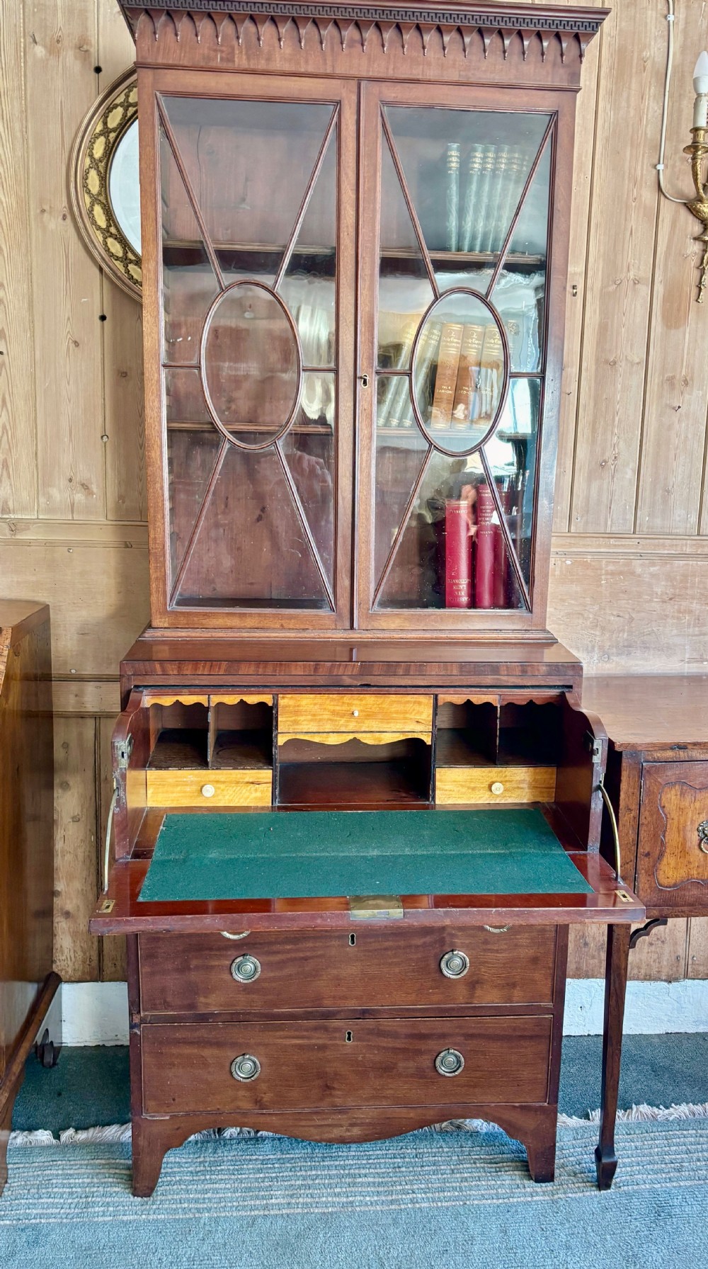 A Regency mahogany secretaire bookcase featuring glazed double doors with geometric astragal glazing above a chest of drawers with brass ring handles. View XV