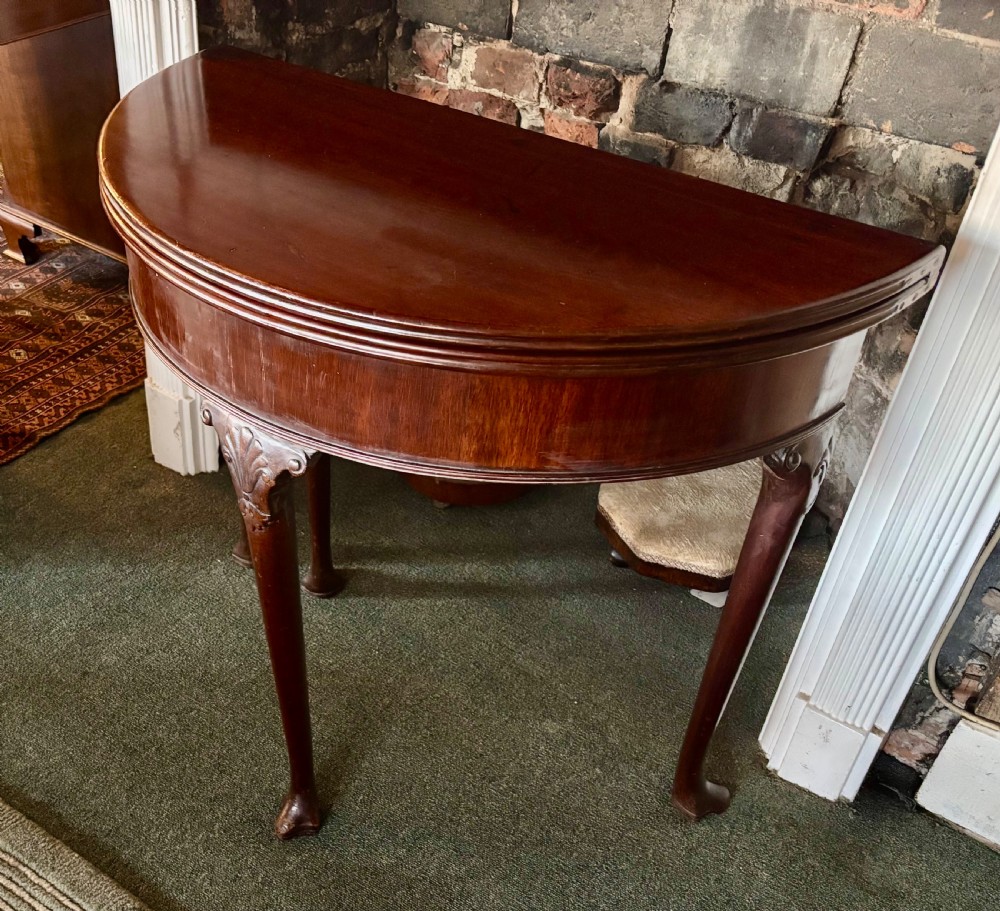 A George III mahogany demi-lune card table with carved shell knees and cabriole legs. View X