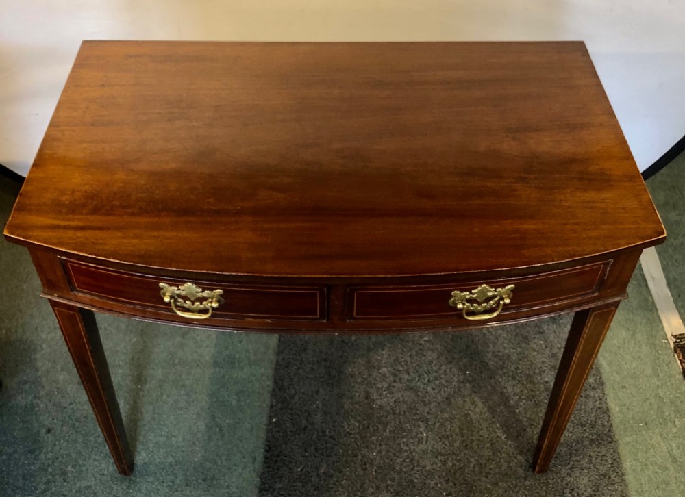 A nineteenth-century mahogany bow-fronted side table featuring two crossbanded drawers with brass handles and tapered legs.