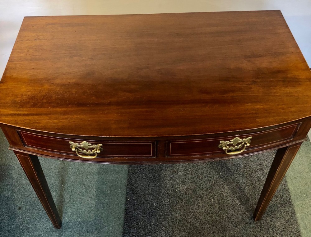 A nineteenth-century mahogany bow-fronted side table featuring two crossbanded drawers with brass handles and tapered legs. View VI