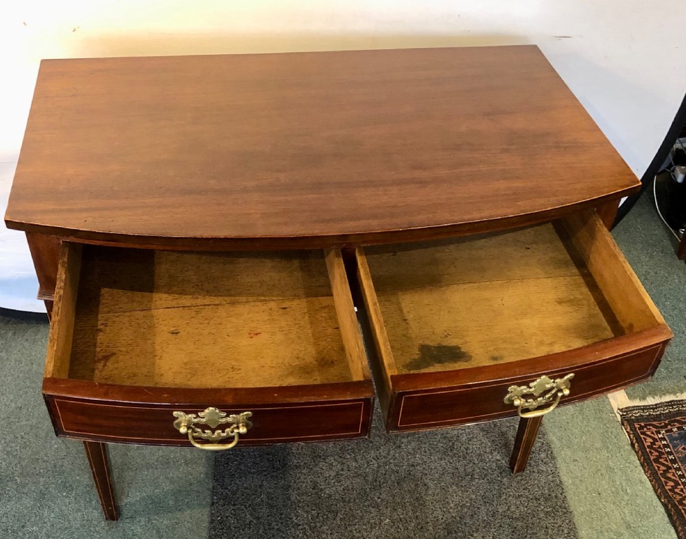 A nineteenth-century mahogany bow-fronted side table featuring two crossbanded drawers with brass handles and tapered legs. View VII