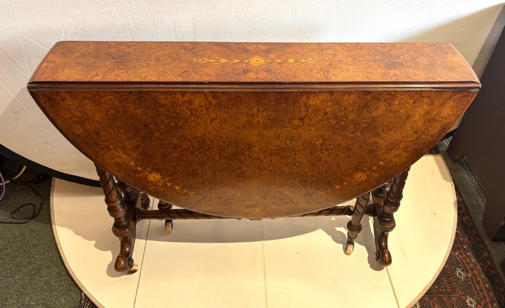 A Victorian burr walnut oval Sutherland table with detailed floral marquetry inlays, turned legs, and drop leaves extended. View IV