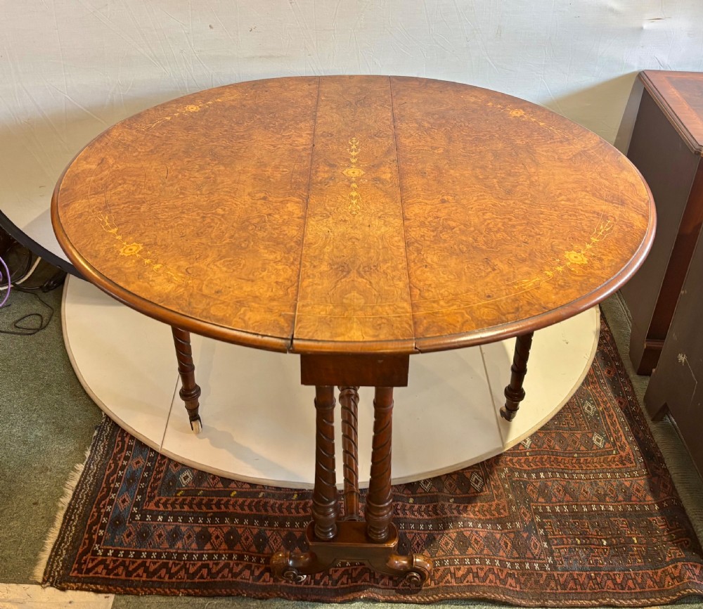 A Victorian burr walnut oval Sutherland table with detailed floral marquetry inlays, turned legs, and drop leaves extended. View VI