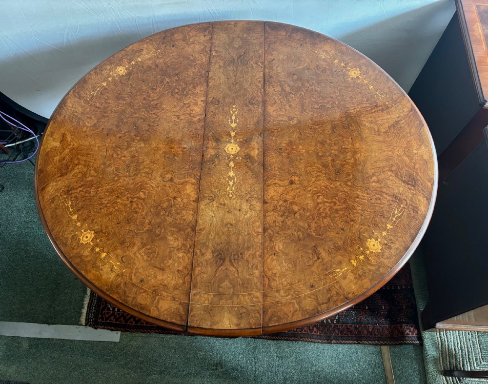A Victorian burr walnut oval Sutherland table with detailed floral marquetry inlays, turned legs, and drop leaves extended. View VII