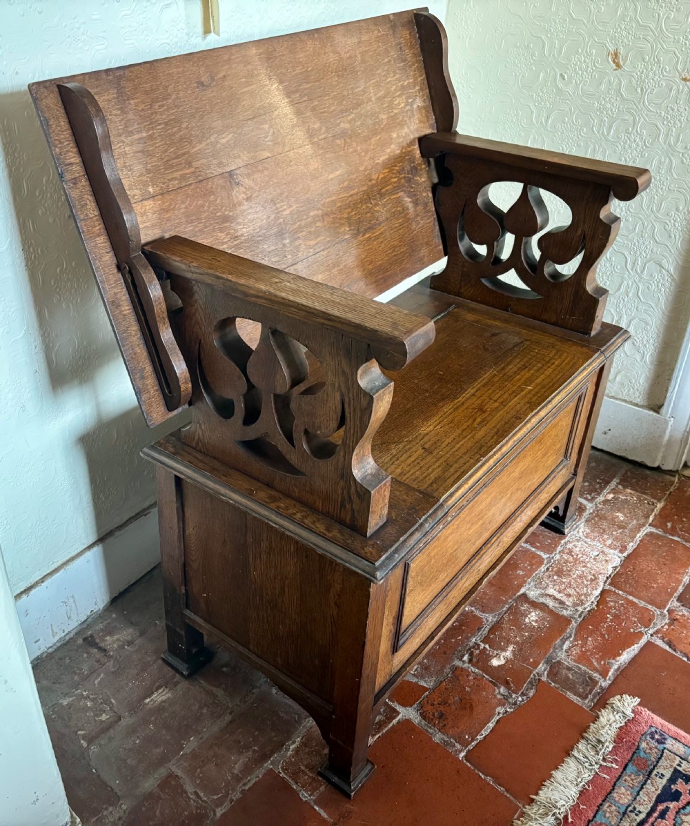 A small oak Art Nouveau monks bench with a hinged flip-top backrest, pierced heart cut-out side supports, and a hinged seat opening to a storage chest. View II