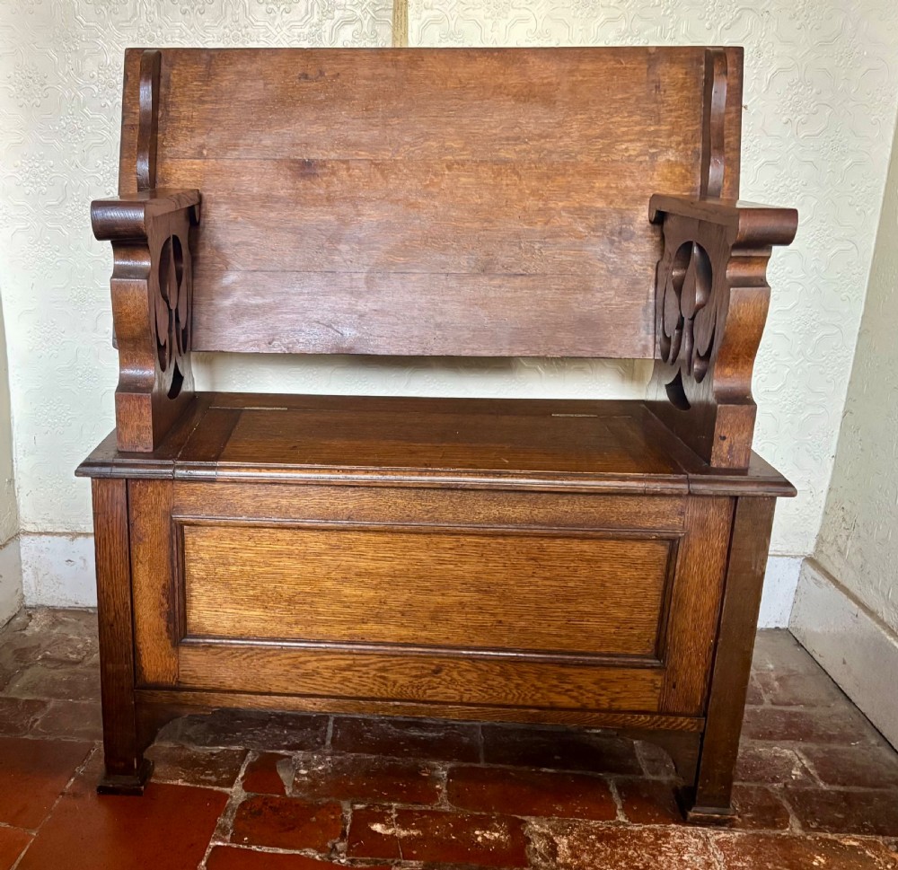 A small oak Art Nouveau monks bench with a hinged flip-top backrest, pierced heart cut-out side supports, and a hinged seat opening to a storage chest. View IV