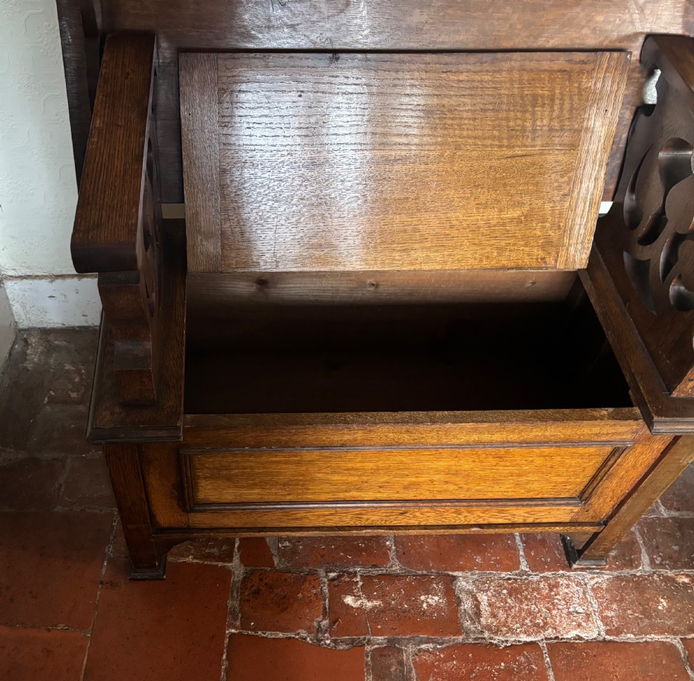 A small oak Art Nouveau monks bench with a hinged flip-top backrest, pierced heart cut-out side supports, and a hinged seat opening to a storage chest. View V