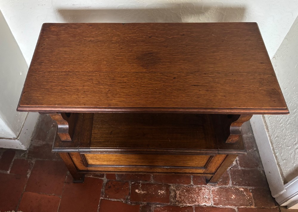 A small oak Art Nouveau monks bench with a hinged flip-top backrest, pierced heart cut-out side supports, and a hinged seat opening to a storage chest. View VI