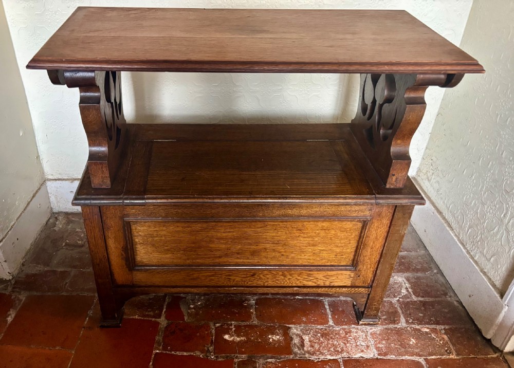 A small oak Art Nouveau monks bench with a hinged flip-top backrest, pierced heart cut-out side supports, and a hinged seat opening to a storage chest. View VII