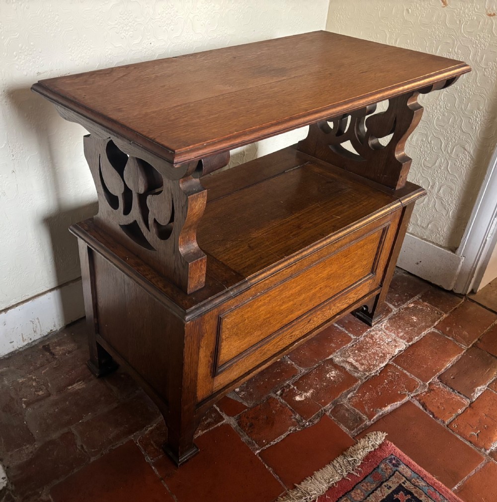 A small oak Art Nouveau monks bench with a hinged flip-top backrest, pierced heart cut-out side supports, and a hinged seat opening to a storage chest. View VIII