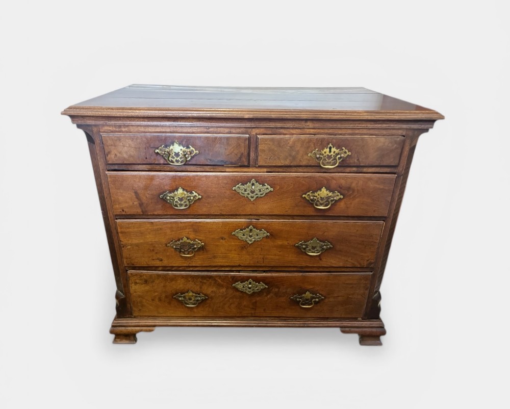 A George III walnut small chest of drawers with decorative brass handles, fluted canted corners, and bracket feet.