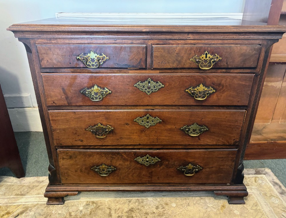 A George III walnut small chest of drawers with decorative brass handles, fluted canted corners, and bracket feet. View XI