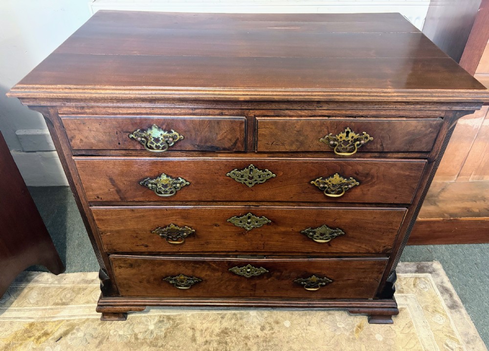 A George III walnut small chest of drawers with decorative brass handles, fluted canted corners, and bracket feet. View XII