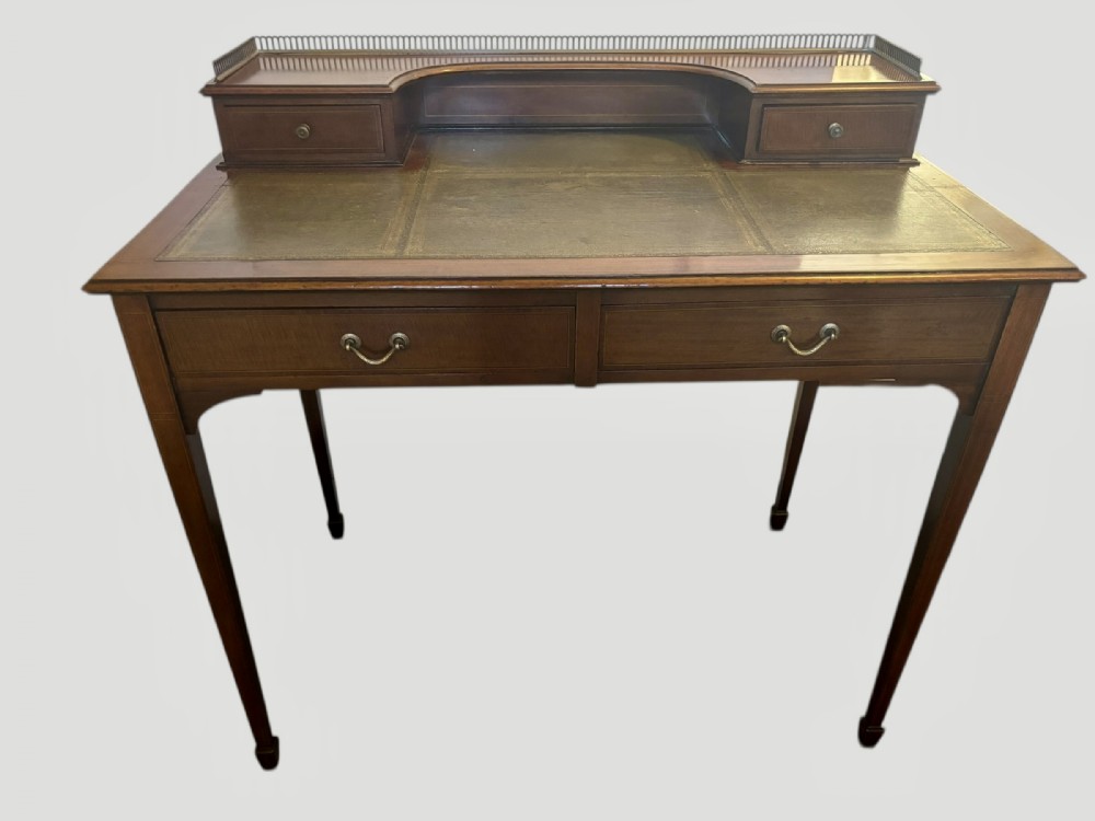 An Edwardian mahogany writing table featuring a green leather inset top, a raised brass gallery superstructure with two small drawers, two frieze drawers, and tapered legs.