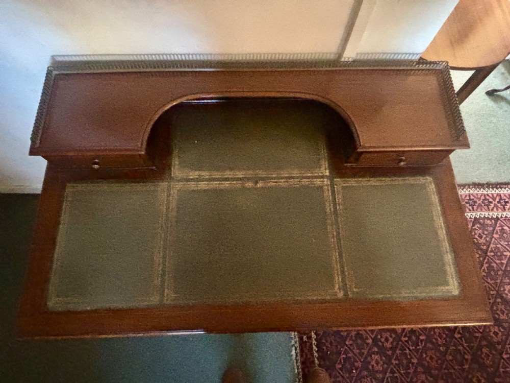 An Edwardian mahogany writing table featuring a green leather inset top, a raised brass gallery superstructure with two small drawers, two frieze drawers, and tapered legs. View VI