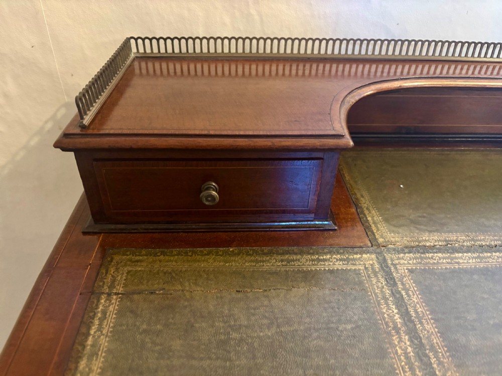 An Edwardian mahogany writing table featuring a green leather inset top, a raised brass gallery superstructure with two small drawers, two frieze drawers, and tapered legs. View VII