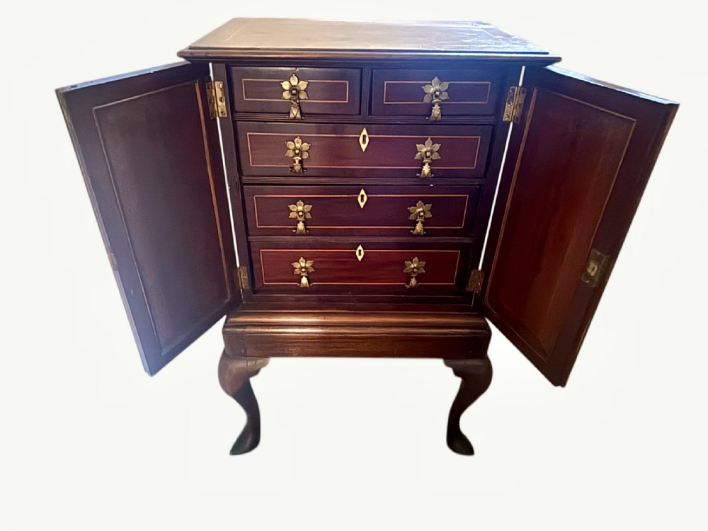 A small 19th-century mahogany cabinet featuring two open outer doors displaying four inlaid drawers with floral brass handles, supported on cabriole legs.