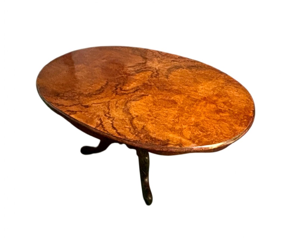 An oval Victorian breakfast table made of polished figured walnut veneer with a central carved pedestal base and splayed legs.