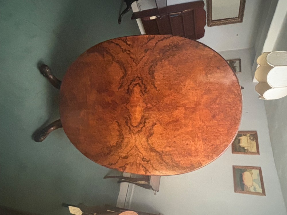 An oval Victorian breakfast table made of polished figured walnut veneer with a central carved pedestal base and splayed legs. View V