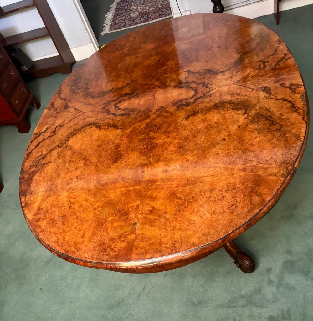 An oval Victorian breakfast table made of polished figured walnut veneer with a central carved pedestal base and splayed legs. View IX