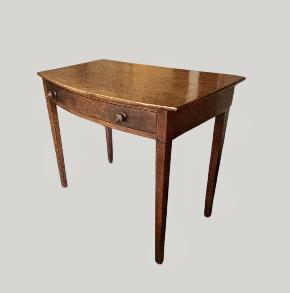 A George III mahogany bow-front side table with a single drawer fitted with turned knobs and four tapered legs.