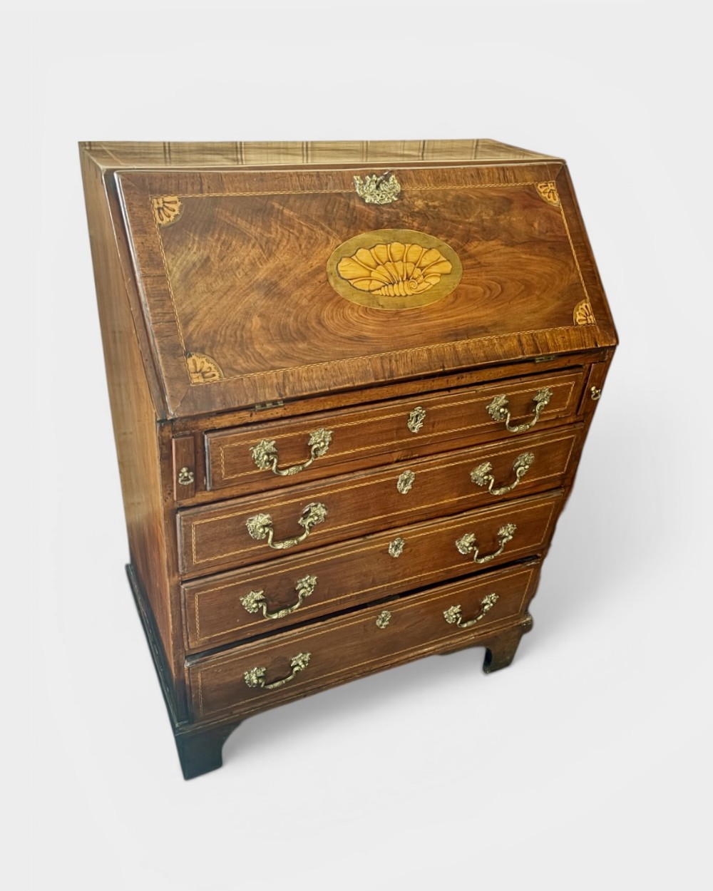 An 18th-century George III mahogany slant-front bureau featuring satinwood shell inlays and four graduating drawers with brass handles.