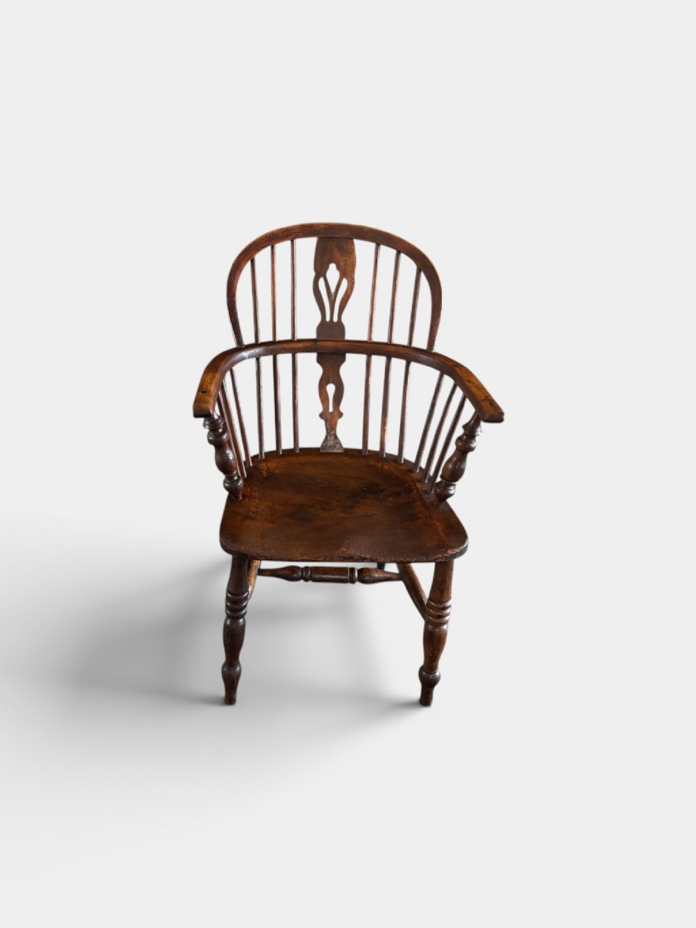 A 19th-century dark elm Windsor armchair featuring a curved hoop back, central pierced splat, turned spindles, curved armrests, shaped seat, and turned legs joined by stretchers. View III