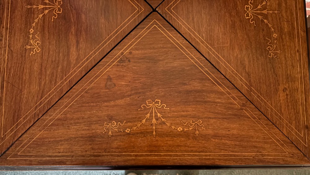 An Edwardian rosewood envelope top card table featuring satinwood inlay and square tapered legs. View V