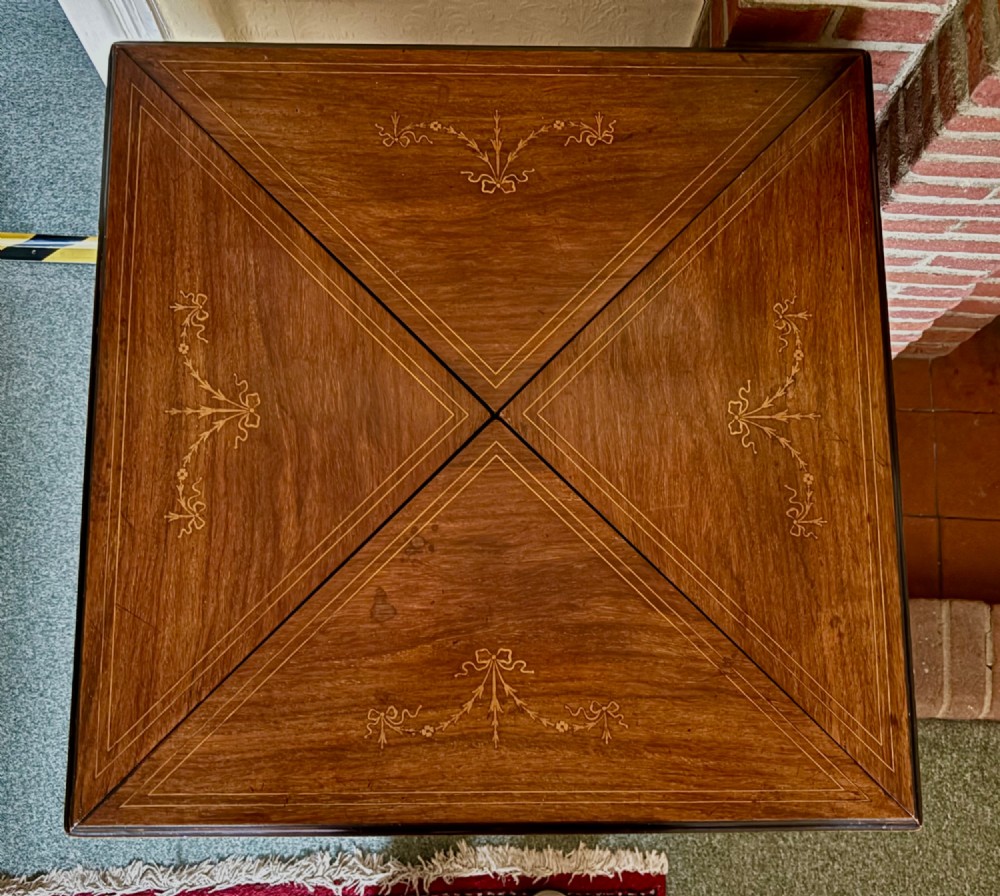 An Edwardian rosewood envelope top card table featuring satinwood inlay and square tapered legs. View VI