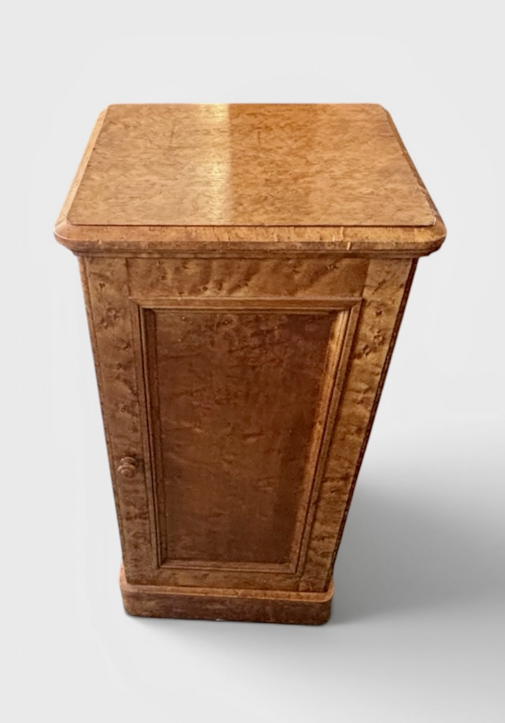 A 19th-century birds eye maple pedestal cupboard featuring a panelled door, turned wooden knob, and plinth base.