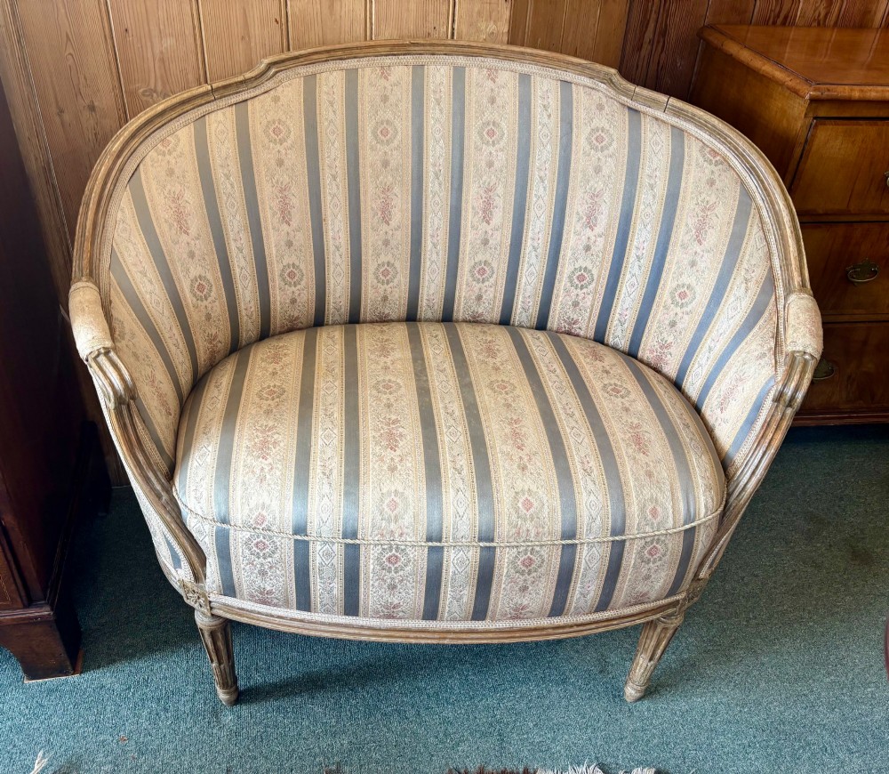 A Louis XVI style small settee featuring a curved barrel back, striped upholstery in grey and blue tones, and carved fluted legs. View II