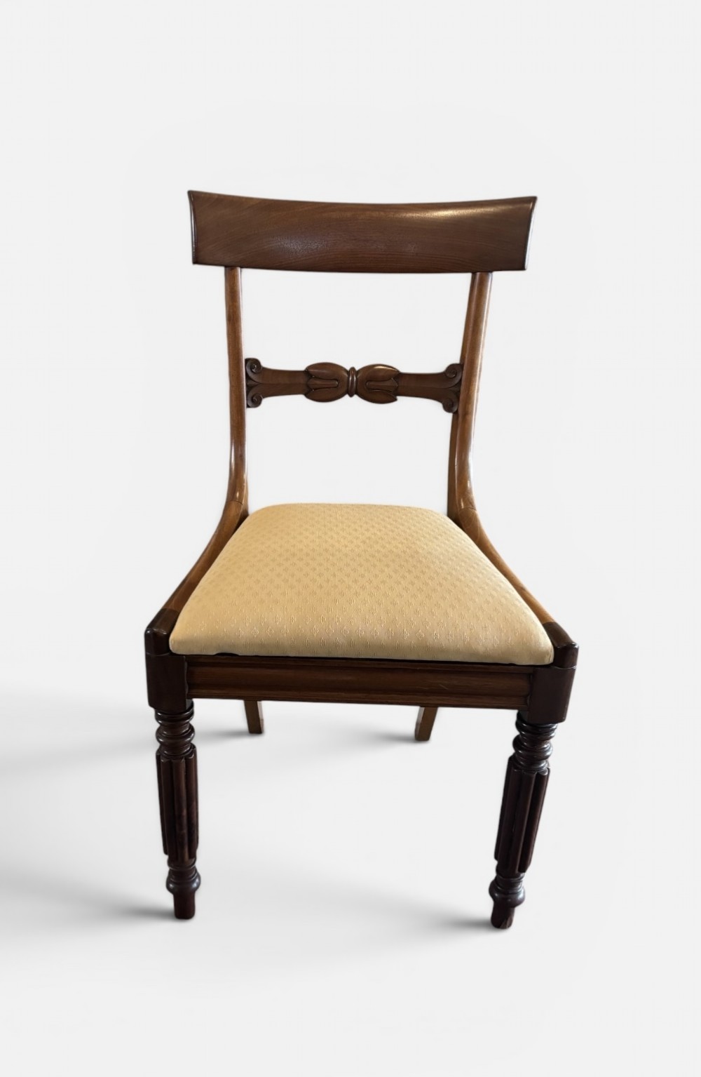 A set of eight 19th-century mahogany dining chairs with curved crest rails, carved central back bars, upholstered seats, and turned front legs. View V