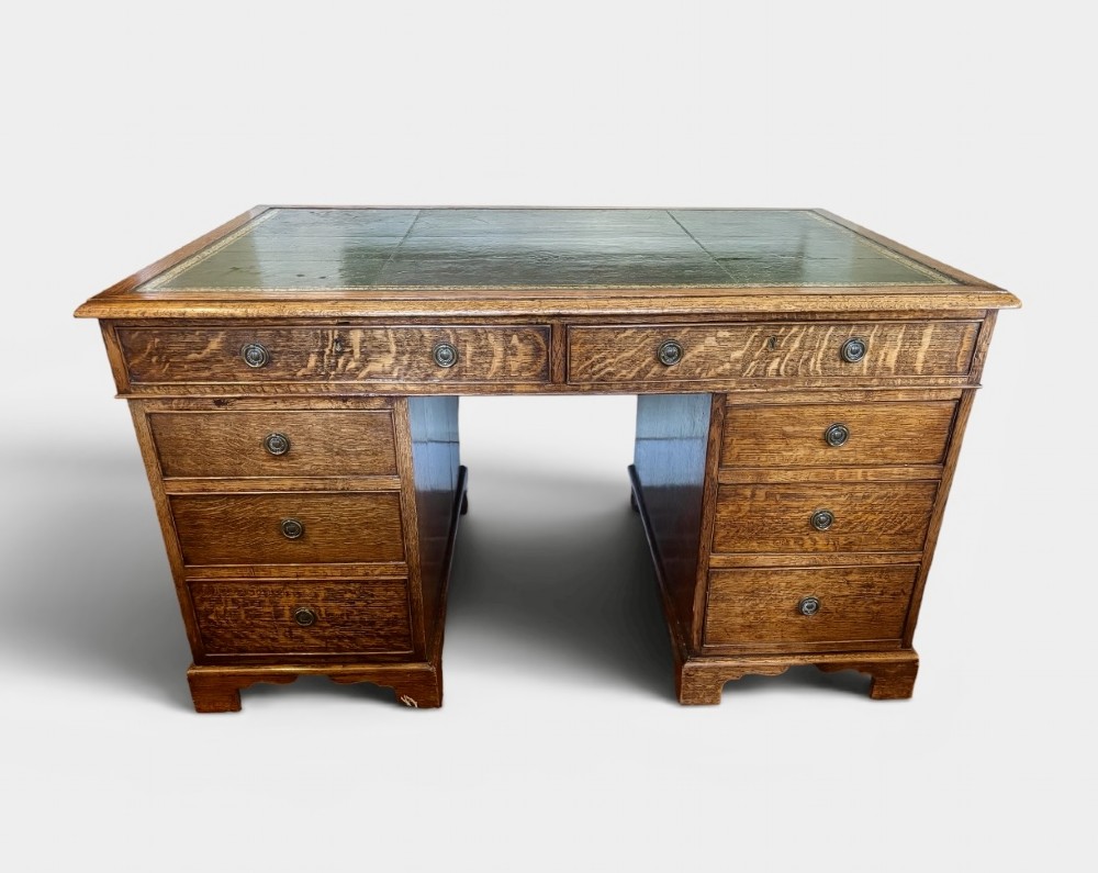 A large Victorian oak pedestal desk featuring a three-panel green leather inset writing top and nine drawers with turned handles.