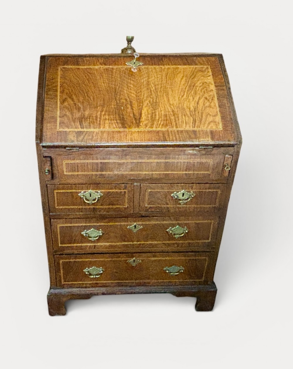 An antique George III walnut slant-front bureau desk featuring brass drop handles, feather-banded inlay, and a graduated drawer base on bracket feet.