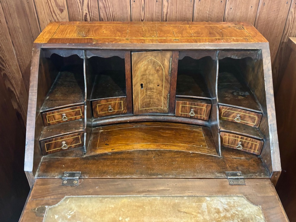 An antique George III walnut slant-front bureau desk featuring brass drop handles, feather-banded inlay, and a graduated drawer base on bracket feet. View II