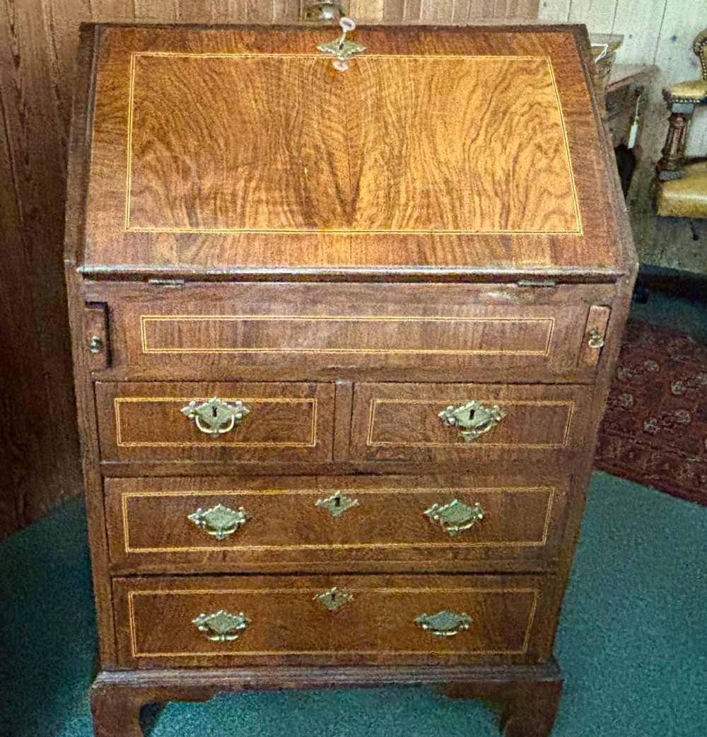 An antique George III walnut slant-front bureau desk featuring brass drop handles, feather-banded inlay, and a graduated drawer base on bracket feet. View V