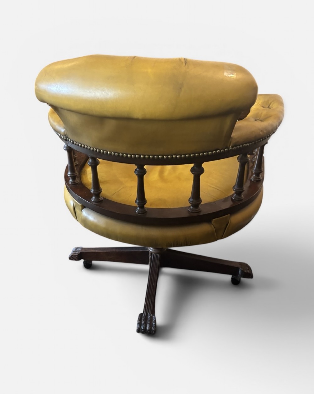 An early 20th-century mahogany revolving desk armchair featuring tan deep-buttoned leather upholstery, turned wooden spindles, brass studding, and a four-legged base on castors. View II