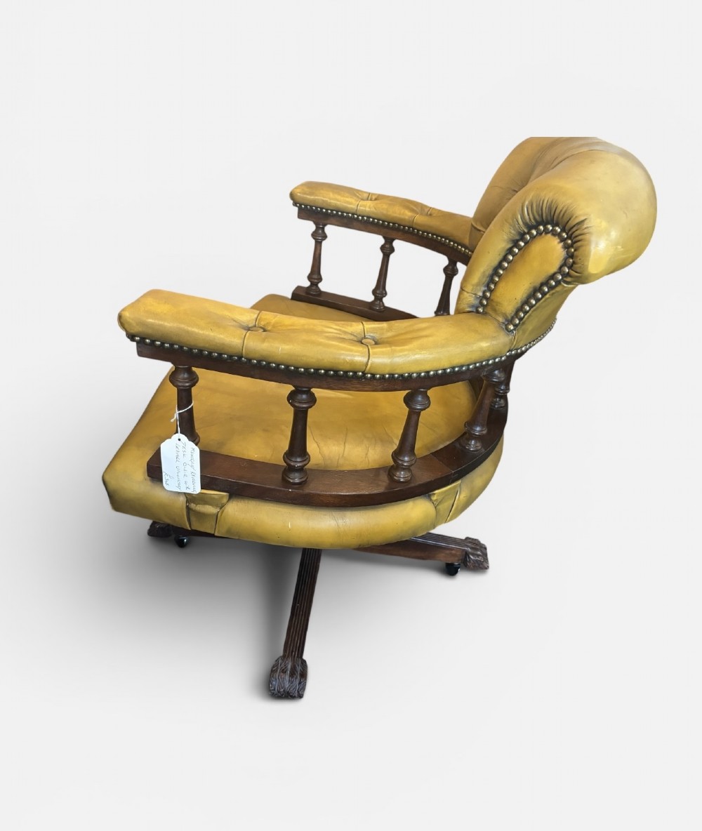An early 20th-century mahogany revolving desk armchair featuring tan deep-buttoned leather upholstery, turned wooden spindles, brass studding, and a four-legged base on castors. View III