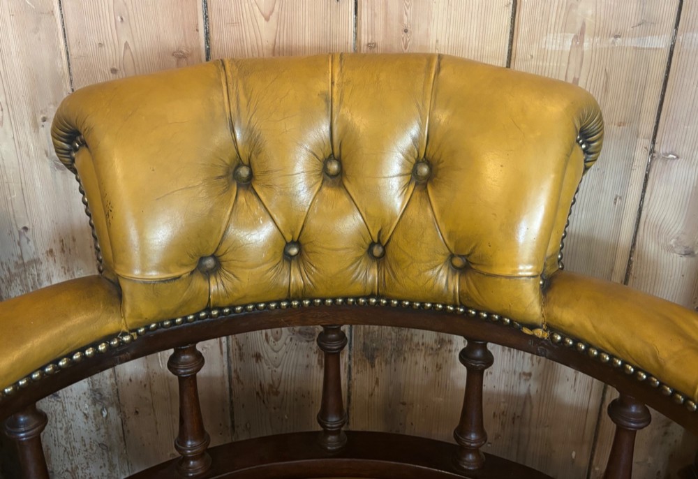An early 20th-century mahogany revolving desk armchair featuring tan deep-buttoned leather upholstery, turned wooden spindles, brass studding, and a four-legged base on castors. View VI