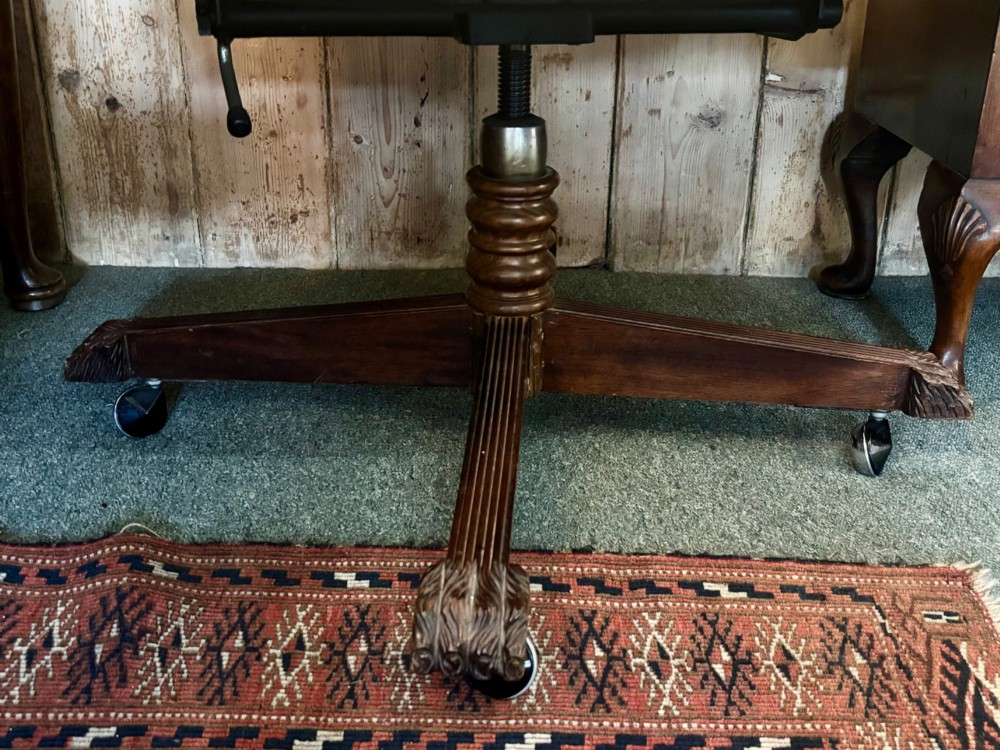An early 20th-century mahogany revolving desk armchair featuring tan deep-buttoned leather upholstery, turned wooden spindles, brass studding, and a four-legged base on castors. View VII