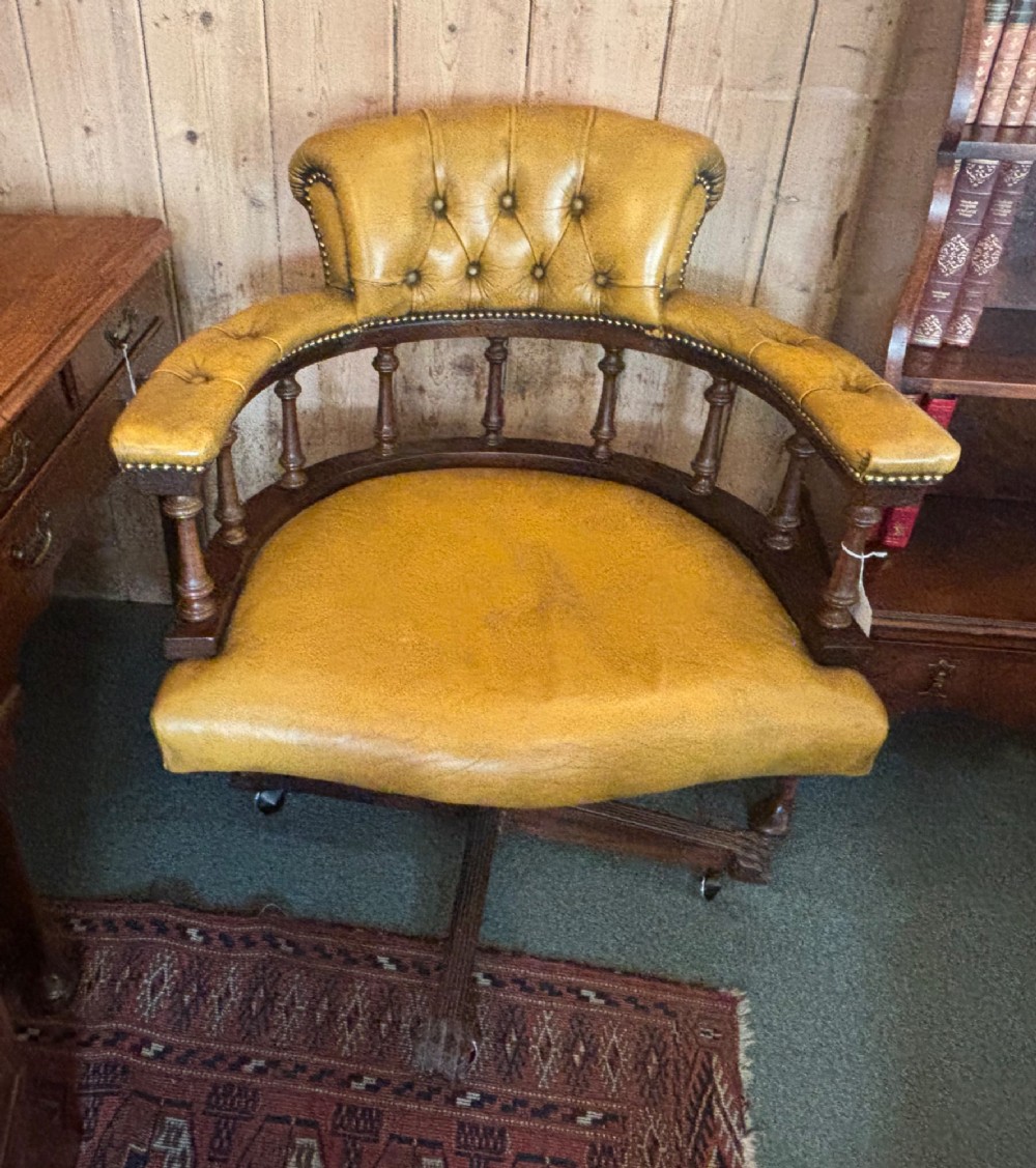 An early 20th-century mahogany revolving desk armchair featuring tan deep-buttoned leather upholstery, turned wooden spindles, brass studding, and a four-legged base on castors. View VIII
