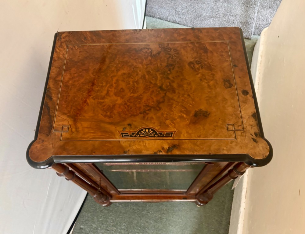 A nineteenth-century Victorian burr walnut music cabinet featuring a single glazed door, turned side pilasters, and internal shelving with embossed leather trim. View IV