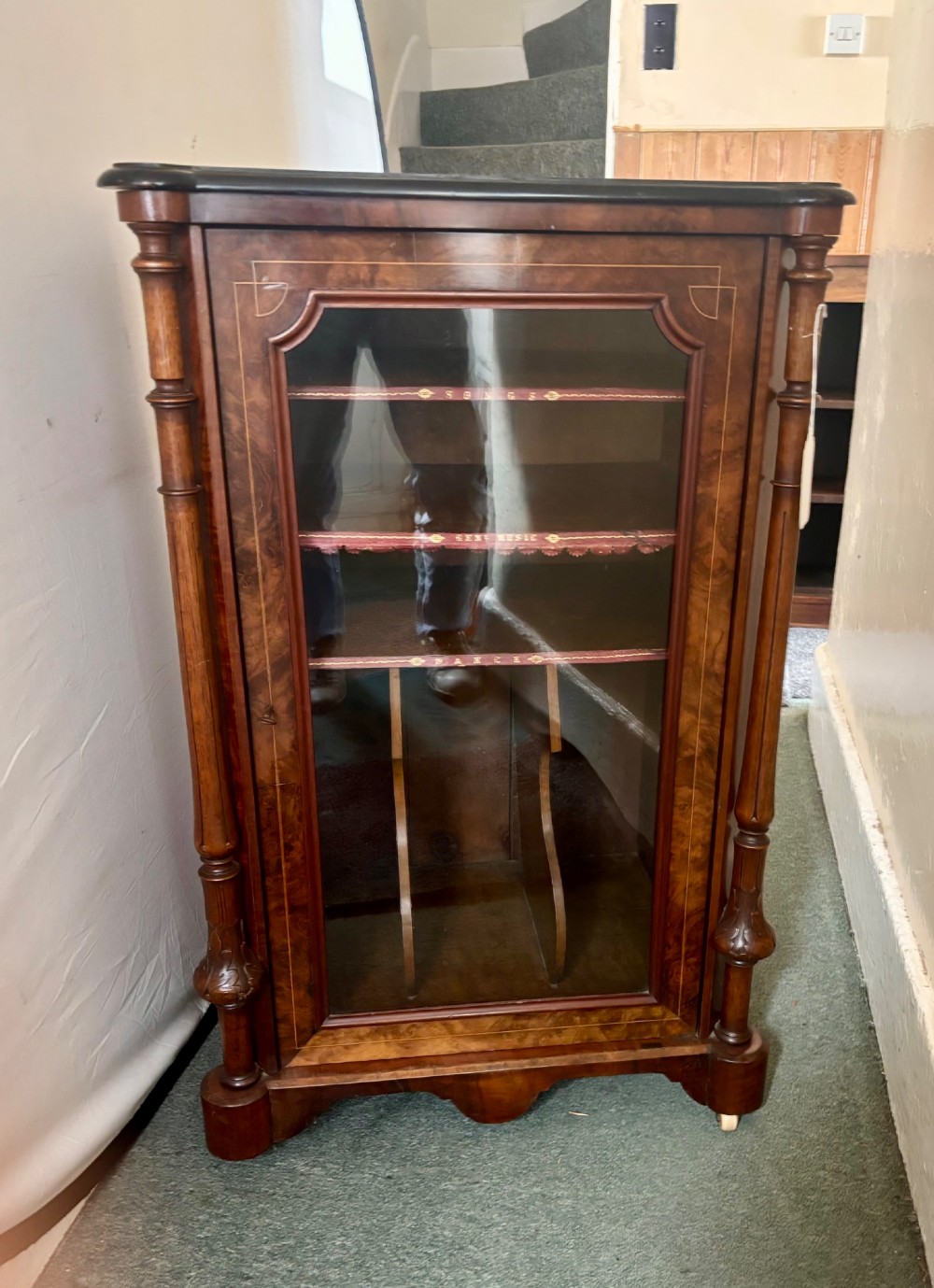 A nineteenth-century Victorian burr walnut music cabinet featuring a single glazed door, turned side pilasters, and internal shelving with embossed leather trim. View V