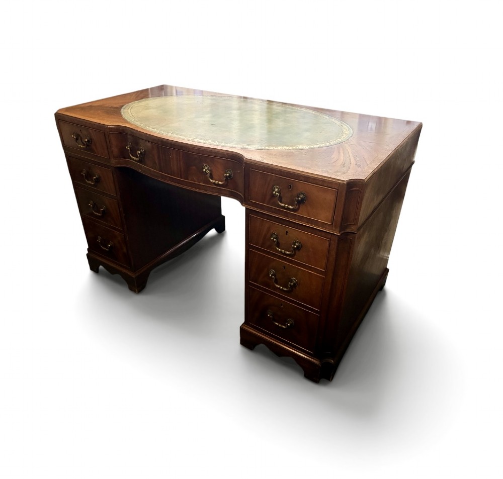 A mahogany pedestal desk featuring an inset green leather top with gilded tooling, brass drop handles, and bracket feet.