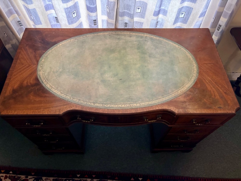 A mahogany pedestal desk featuring an inset green leather top with gilded tooling, brass drop handles, and bracket feet. View V