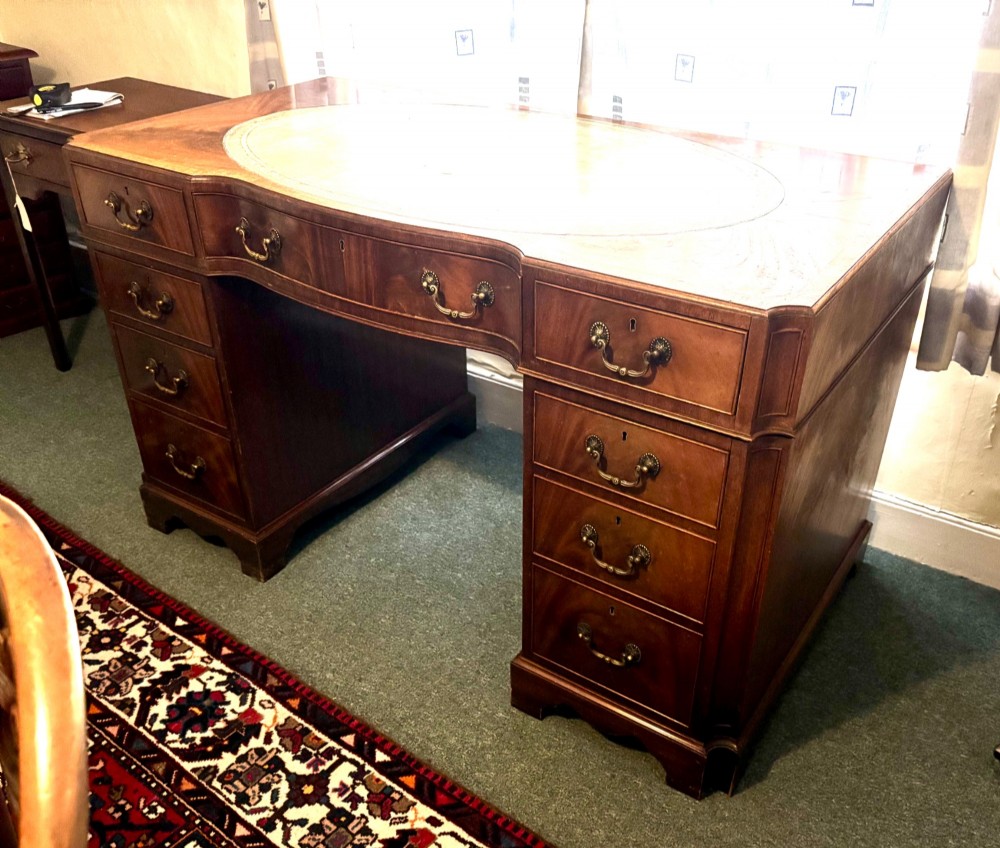 A mahogany pedestal desk featuring an inset green leather top with gilded tooling, brass drop handles, and bracket feet. View VI