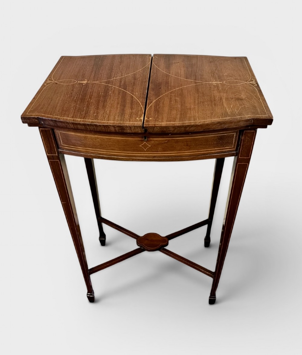 A small Edwardian mahogany work table featuring dual hinged top flaps with delicate satinwood inlay, tapered legs, and an X-frame stretcher.