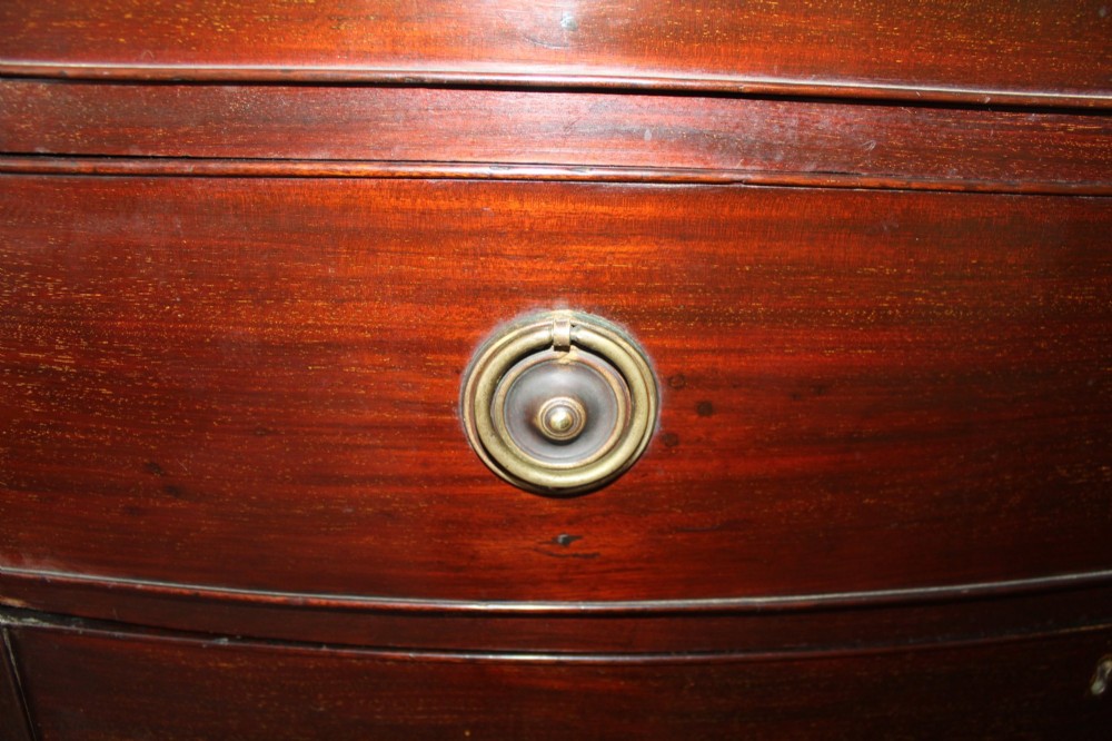 A Regency mahogany bow-front chest of drawers featuring two short drawers over three long graduated drawers with circular brass drop ring handles and splayed bracket feet. View V
