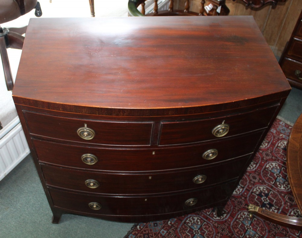 A Regency mahogany bow-front chest of drawers featuring two short drawers over three long graduated drawers with circular brass drop ring handles and splayed bracket feet. View VI