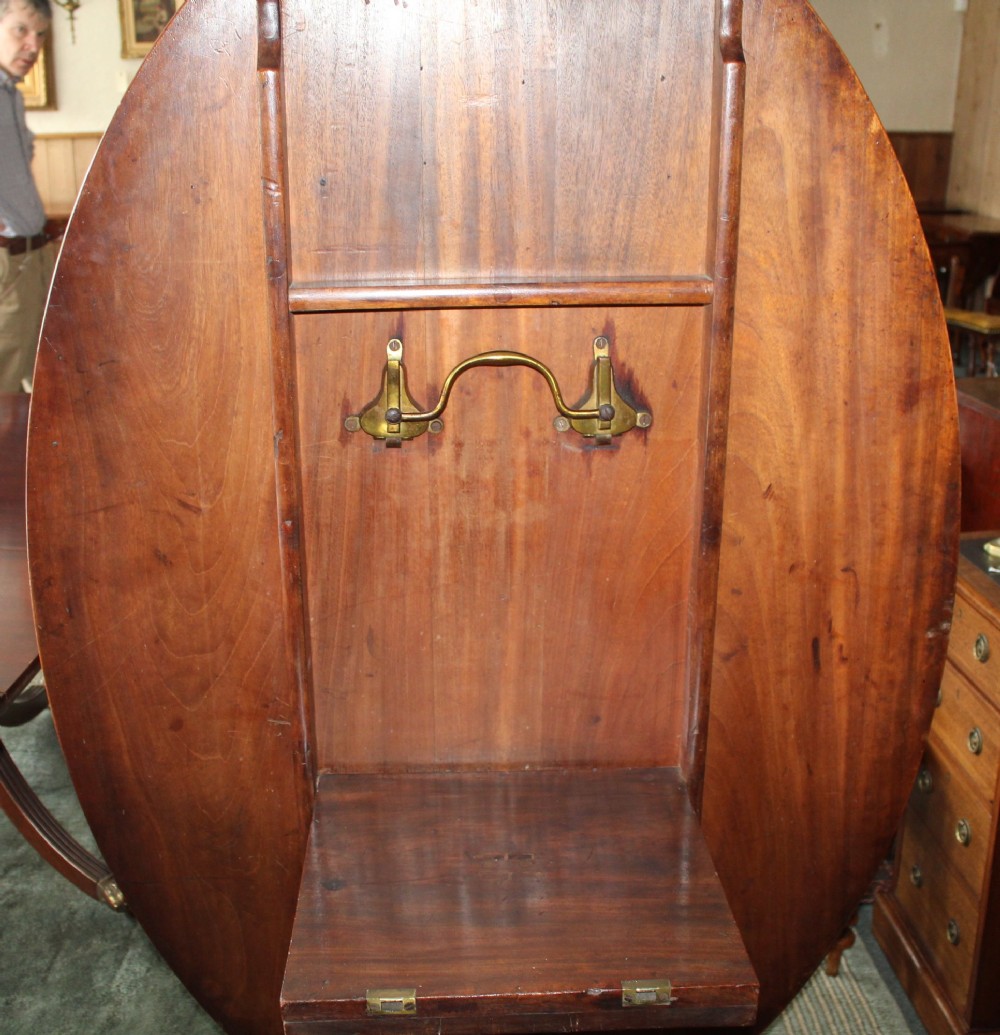 A Regency period oval mahogany breakfast table featuring a figured timber top supported by a central turned pedestal with four reeded legs ending in brass castors. View III